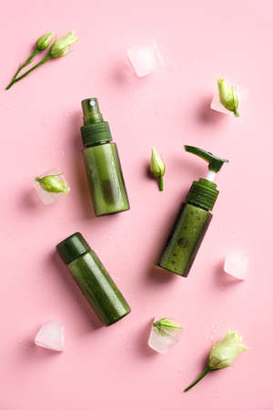 Green cosmetic containers, flowers, ice cubes on pink background. Natural beauty products concept.の写真素材