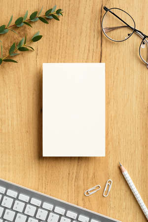 Wood desk table with blank paper note mockup, keyboard, glasses, office supplies, eucalyptus leaves. Flat lay, top view.の写真素材