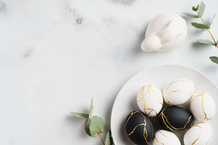 Elegant Easter flat lay composition. Black and golden Easter eggs, rabbit bunny, eucalyptus leaves on marble background. Top view with copy space. Happy Easter concept. Minimal style.の写真素材