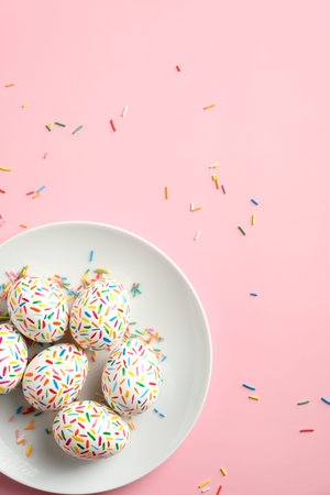 Colorful Easter eggs in plate on pastel pink background. Happy Easter concept. Flat lay, top view.