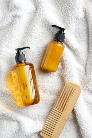 Hair care products design. Yellow dispenser bottles with shampoo and lotion, wooden hair comb on white towel in bathroom. SPA cosmetics packaging mockup, brandingの写真素材