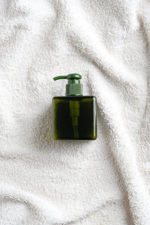 Green glass shampoo or soap dispenser bottle on white towel in bathroom. SPA natural organic beauty...
