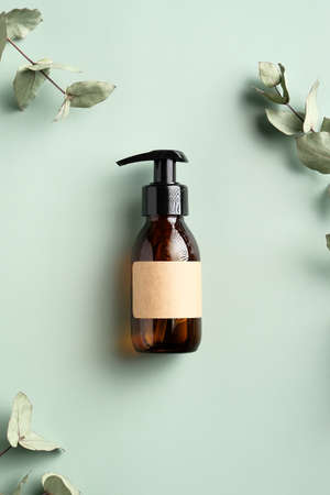 Dark amber glass dispenser bottle with homemade shampoo and eucalyptus leaves on green background. SPA natural organic cosmetic product packaging design, branding.の写真素材