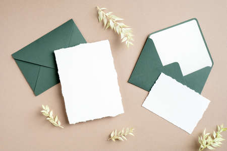 Elegant wedding stationery set. Wedding invitation card mockup, green envelopes, dried flowers on pastel beige background. Flat lay, top view, copy space.の写真素材