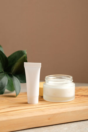 Set of white cosmetic lotion tube and jar of moisturizer cream on wooden board with green leaf....