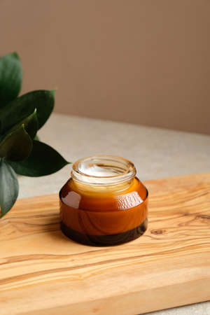 Amber glass jar of moisturizer cream on wooden board and green leaf. Natural organic skincare product, body lotion, face cream.の写真素材