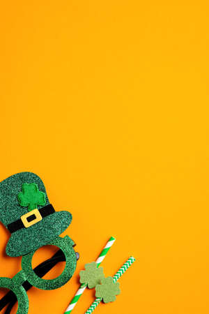 Saint Patrick's Day minimal concept. Festive party glasses and drinking straws on orange background. Flat lay, top view. Happy St Patricks Day banner design.の写真素材
