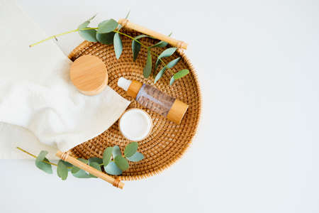 SPA natural organic cosmetics set in rattan tray on table in bathroom. Jar of moisturizer cream, body lotion, eucalyptus leaves, towel. Flat lay, top view.の写真素材