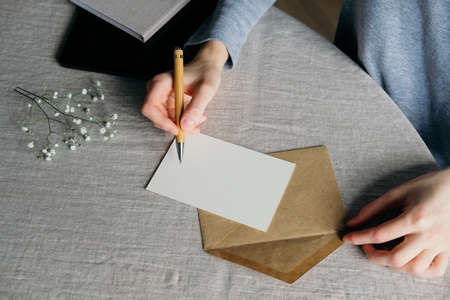 Closeup woman writing letter or wedding invitation card on table with linen tablecloth. Love, romance concept.の写真素材