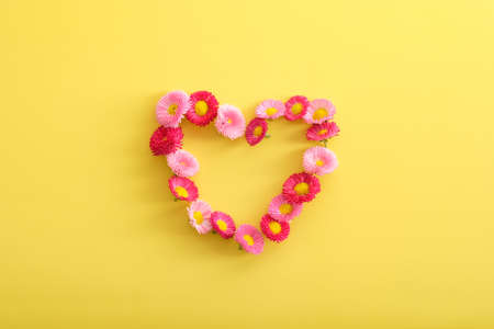 Heart shape made of flowers on yellow background. Love, romance concept. Creative flat lay composition, top view. Greeting card for Mother's Day, Birthday, Women's Dayの写真素材