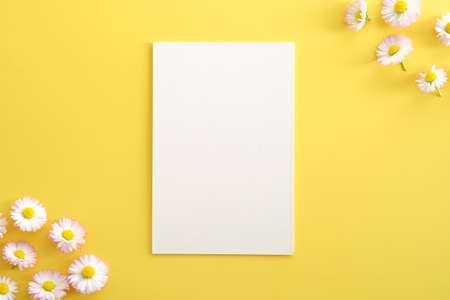 Blank paper card mockup and chamomiles on yellow background. Flat lay, top view, copy space.の写真素材