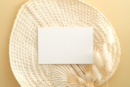 White invitation card mockup with lagurus on rattan fan on beige backround. Flat lay, top view, minimal style.の写真素材