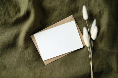 White invitation card mockup with dried flowers on vintage green fabric. Romantic letter, wedding invite card. Flat lay, top view.の写真素材