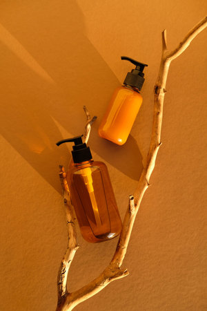 Amber glass cosmetic bottles on wooden branch in sunlight of sunset. Flat lay, top view. Natural...