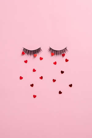 False eye lashes and confetti on pink background top view. Creative flat lay composition with makeup cosmetics.の写真素材