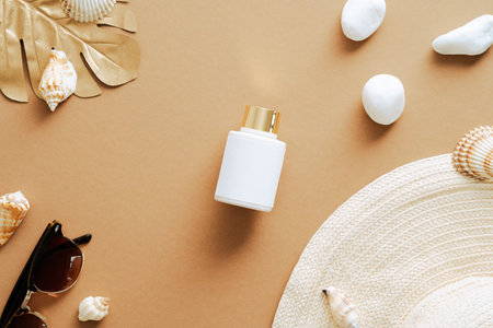 Flat lay composition with sunscreen lotion, straw hat, seashells, sunglasses on sand colored...