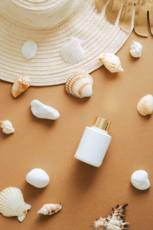 Suntan lotion bottle, seashells, straw hat on sand colored background. Flat lay, top view, copy space. Sunscreen beauty product packaging designの写真素材
