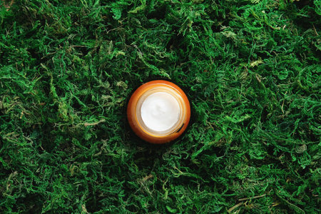 Amber glass jar of moisturizer cream on moss background in forest. Natural eco-friendly beauty...