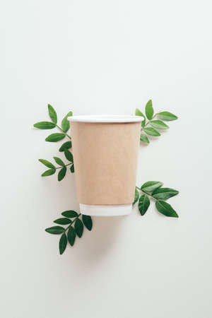Eco-friendly disposable coffee cup with green leaves on white background, Zero waste, plastic free, sustainable lifestyle concept.の写真素材