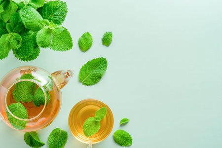 Flat lay mint tea in teapot and cup on green background. Herbal tea concept.
