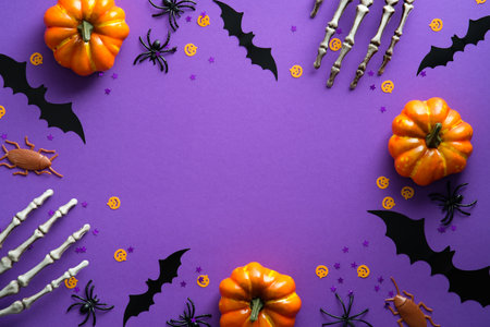 Happy Halloween holiday concept. Halloween decorations, skeleton hands, bats, pumpkins on purple background. Halloween party greeting card mockup with copy space. Flat lay, top view, overhead.の写真素材