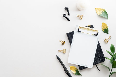 White office desk table with blank clipboard, earphones, office supplies and fall leaves. Elegant...