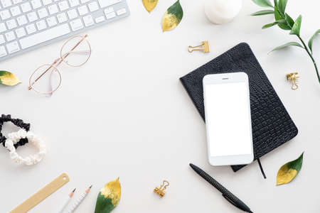 Feminine desk table with mobile phone mockup, notebook, keyboard, office supplies on white background. Flat lay, top view. Elegant workspace.の写真素材