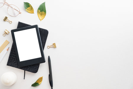E book digital tablet mockup, paper notebook, pen, candle and green leaves on white desk table. Flat lay, top view, overhead.の写真素材