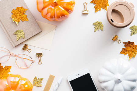 Autumn feminine workspace. Home office desk table with notebook, smartphone, pumpkins, cup of coffee on white background. Flat lay, top view. Cozy, hygge styleの写真素材