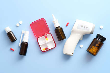 Medical tools and medication on pastel blue background. Flat lay digital thermometer, first aid kit, nasal spray, pills.の写真素材