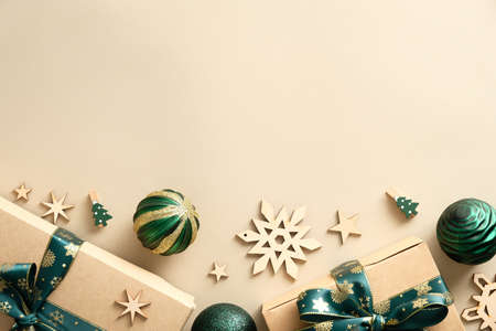 Christmas wooden natural decorations, green balls, gifts wrapped craft paper on pastel beige background. Christmas greeting design. Flat lay, top view, copy space.の写真素材
