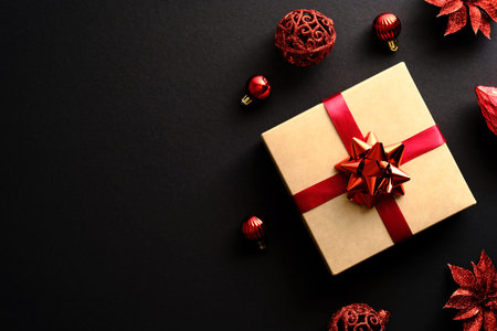 Elegant Christmas gift box with red ribbon, red decorations, balls on black background. Christmas...