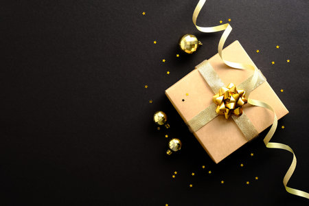 Stylish Christmas gift with golden balls, party streamer ribbon, confetti on dark black background. Christmas, Black friday, Birthday conceptの写真素材