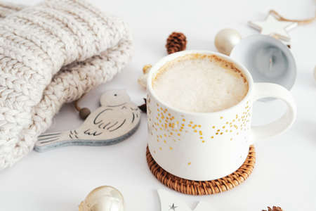 Cup of hot chocolate or coffee, knitted hat, nordic style Christmas decorations on white table desk. Scandinavian aesthetic, Hygge, cozy homeの写真素材
