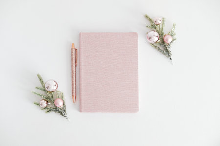 Pink notebook with pen and Christmas tree branches decorated pink balls on white background. Elegant Christmas feminine workspace top view.の写真素材