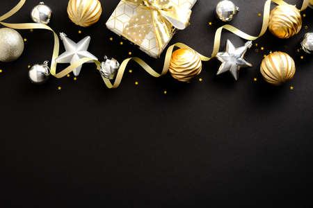 Christmas composition. Golden and silver Christmas stars and balls decoration, gift box on dark black background. Christmas or New Year greeting card design. Flat lay, top view, copy space.の写真素材