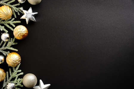Golden and silver Christmas baubles and stars decoration with fir branches on black background with copy space. Merry Christmas and Happy New Year greeting card. Minimal style. Flat lay, top view.の写真素材