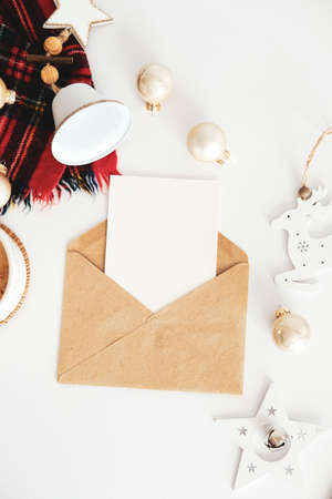 Christmas letter mockup. Craft paper envelope with blank paper card and Xmas decorations on white table. Flat lay, top view, copy space.の写真素材