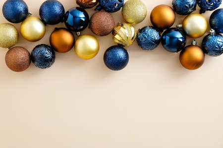 Colorful Christmas baubles decoration frame border on pastel beige background. Flat lay blue, golden and bronze Xmas balls top view.の写真素材