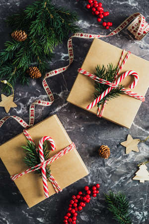 Festive Christmas composition. Craft paper gift boxes decorated striped ribbon, fir branch and candy cane on stone table. Flat lay, top view, overhead.の写真素材