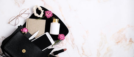 Elegant women's handbag with smartphone, paper notebook, scrunchy, lotion, glasses on marble table....