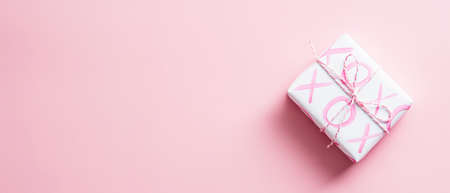 Happy Valentines day banner design with gift box. Gift box wrapped white paper with sign XO on pink background. Top view, copy space.の写真素材