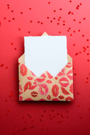 Envelope with lipstick marks and blank paper note inside on red background, top view. Romantic, Love letter concept. Happy Valentines Day greeting card mockup.の写真素材