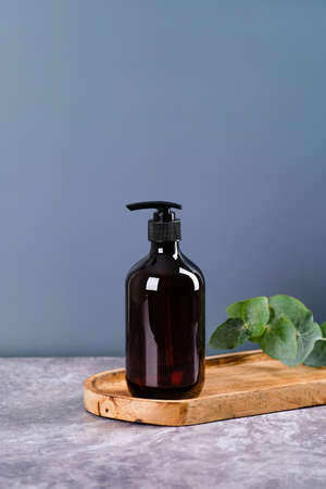 Dark brown amber glass dispenser bottle with shower gel o, eucalyptus leaves on wooden board. SPA natural beauty product designの写真素材