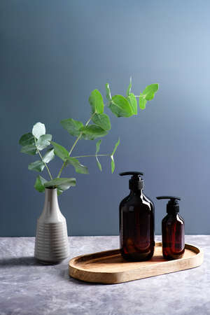 Dark brown amber glass bottles and vase with eucalyptus plant on blue background. SPA natural beauty products design.の写真素材