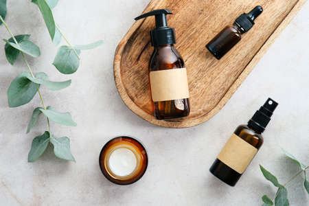 Dark amber glass cosmetic bottles with blank labels and eucalyptus green leaves on stone table. Flat lay, top view.の写真素材