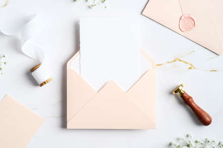 Wedding invitation card mockup inside pastel pink envelope with wax seal stamp, ribbon, flowers on marble table. Wedding stationery set.の写真素材