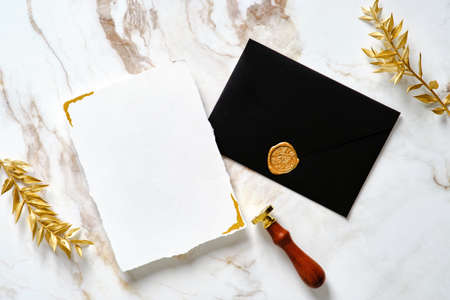 Luxury wedding invitation card mockup with black envelope, gold wax seal stamp, golden leaves on marble gold table. Flat lay, top view, copy space.の写真素材