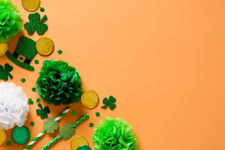 St Patricks Day party decorations on orange background. Flat lay drinking straws, leprechauns hats, shamrock clover leaves confetti, decor. Happy Saint Patricks Day banner design, greeting cardの写真素材