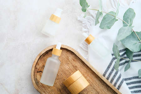 Natural SPA cosmetics in transparent glass packaging with eucalyptus leaves and towel on stone table in bathroom. Flat lay, top view.の写真素材